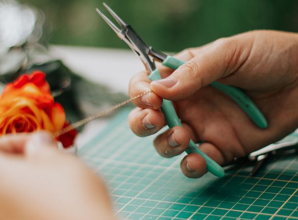 Mains d'artisane travaillant avec des pinces sur une chaîne dorée, étapes de création des bijoux L'Atelier d'Auriane.