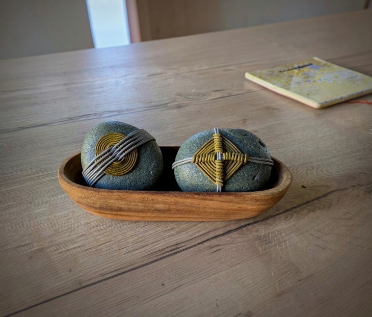 deux galets décorés de fil en cuir, posés dans une petite coupelle en bois sur une table
