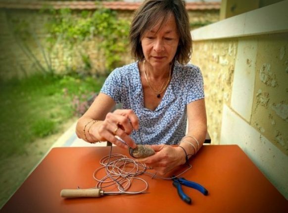 femme fabriquant un caillou tresé avec du fil de cuir.