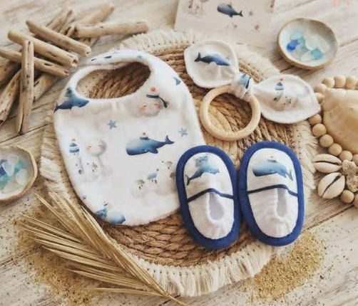 Accessoires artisanaux pour bébé sur le thème marin avec bavoir, anneau de dentition et chaussons baleines bleues.