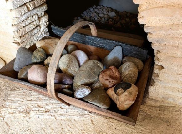 panier en bois rempli de galets et de pierres naturelles de différentes formes et couleur, posé près d'une cheminée en pierre